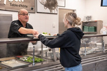 Homme servant de la nourriture à une femme au comptoire alimentaire.