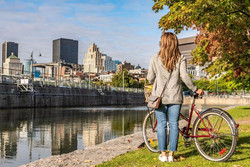 Femme debout à côté de son vélo, face à l'eau et la vue du centre-ville de Montréal.