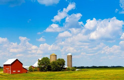 Ferme avec silos au vaste champs et ciel bleu nuagé.
