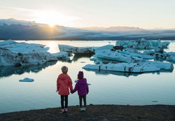 Deux enfants se tenant la main devant l'eau et les glaciers.
