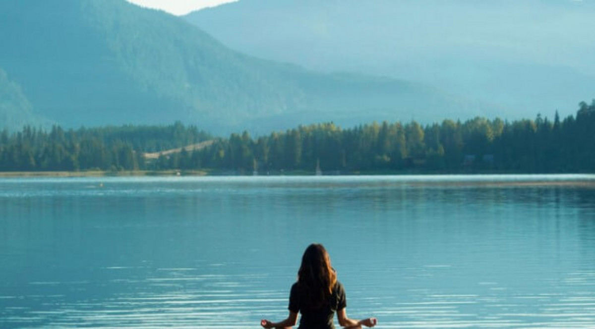 Femme méditant face à un lac.